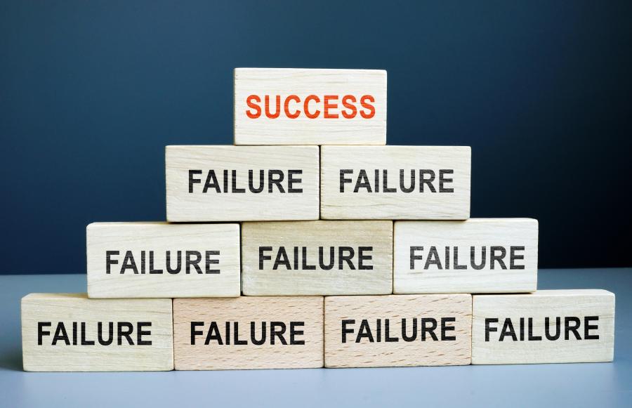 A pyramid of stacked blocks all with the word failure on them except the pinnacle box, which holds the word success.